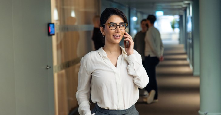 Kvinna pratar i mobil i kontorsmiljö.