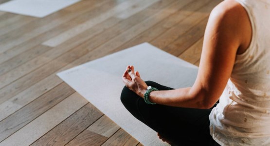 En kvinna sitter på en yogamatta och mediterar.