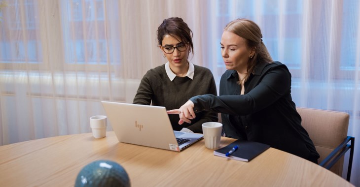 Två kvinnor i möte, tittar på något tillsammans på en laptop.