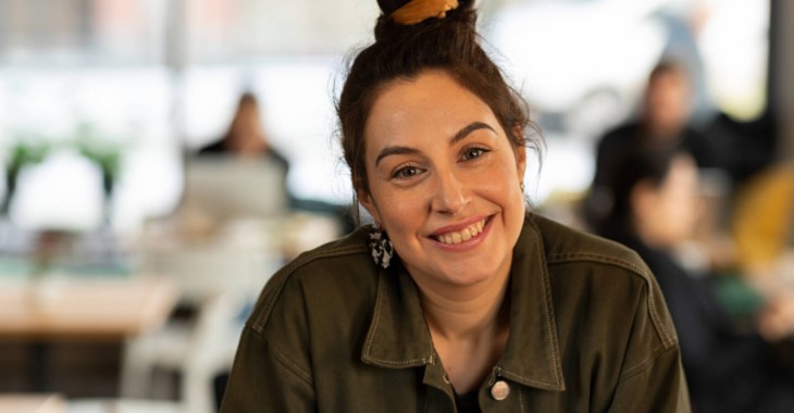 En kvinna som sitter i ett kontorslandskap som ler direkt mot kameran.