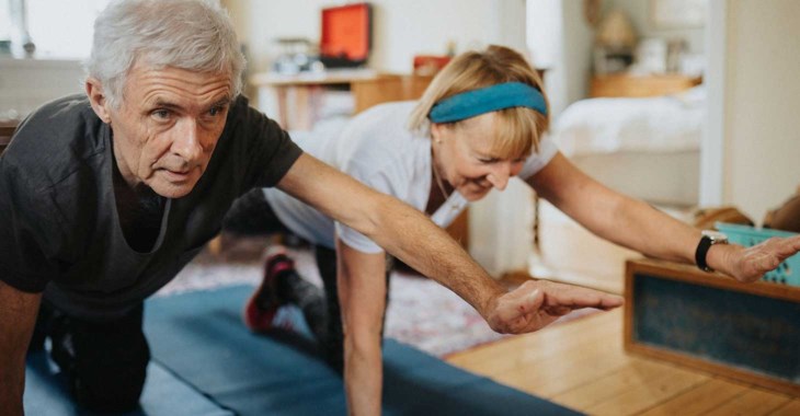 Par i medelåldern gör yogaövningar hemma.
