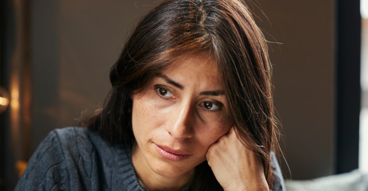 En kvinna som lutar huvudet mot handen och ser lite nedstämd ut.