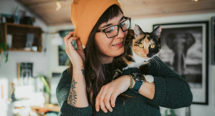 En kvinna håller sin sköldpaddsfärgade katt på axeln.