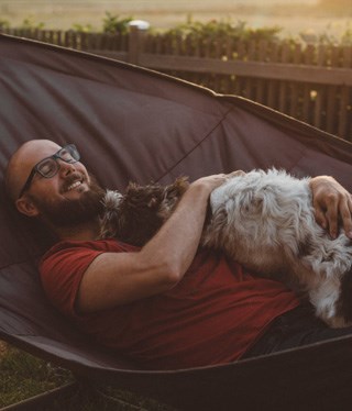 Person ligger i hängmattan med sin hund.
