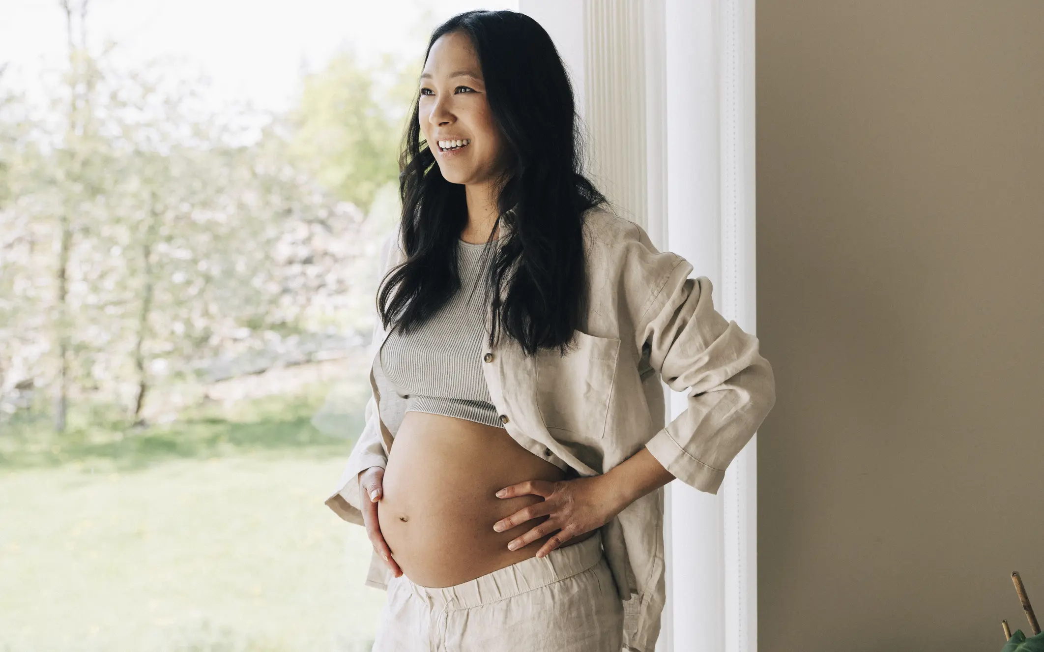 Gravid kvinna står vid fönster.