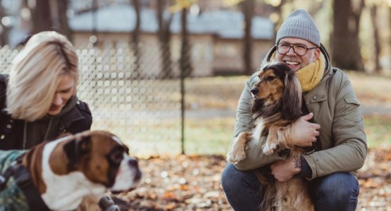 En husse och en matte kramar om sina hundar i en rastgård.