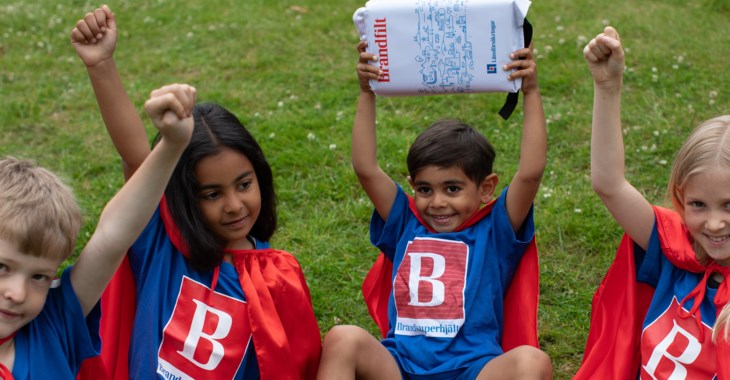 Fyra brandsuperhjältar sitter i gräset med uppsträckta armar.