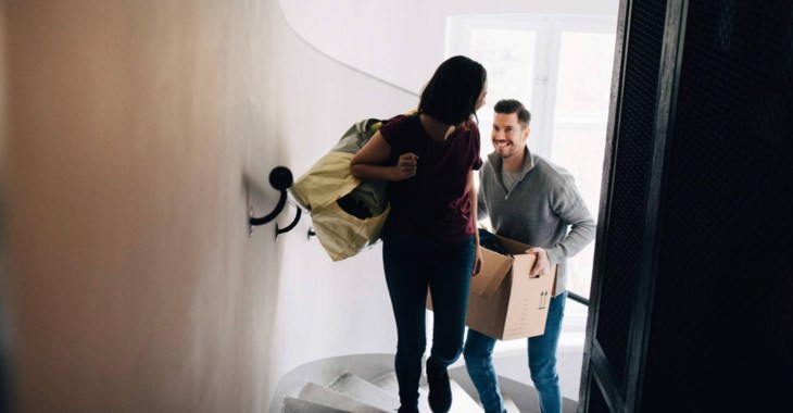 Ett par bär flyttlådor upp i ett trapphus.