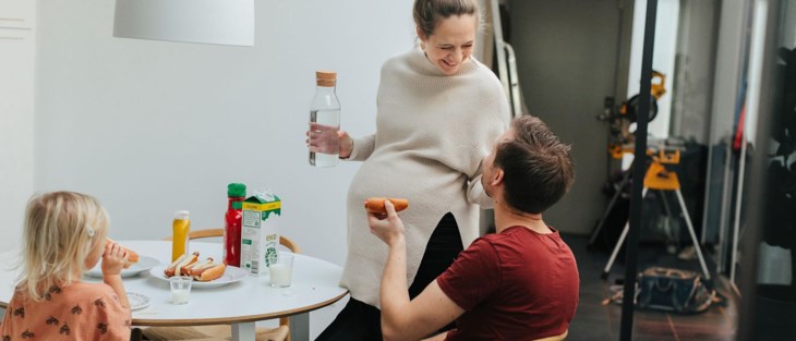 Familj äter korv med bröd vid köksbordet.