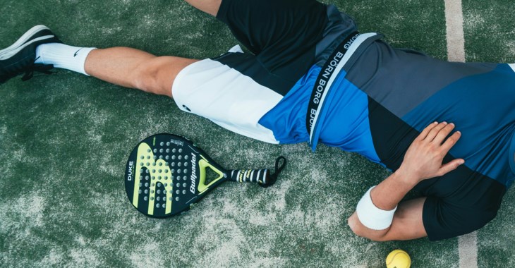 Kille som ligger utslagen på en padelbana.