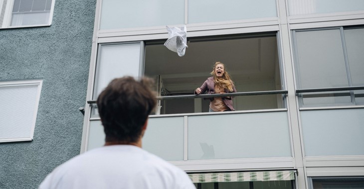 Kvinna kastar ut saker från balkong, man står nedanför.