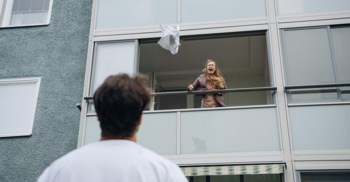 Kvinna kastar ut saker från balkong, man står nedanför.