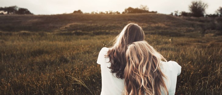 Två tjejer sitter på äng