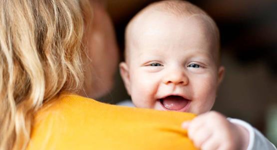 En glad bebis kikar över sin mammas axel.