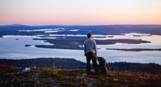 Man stående på ett fjäll och ser ut över solnedgången.