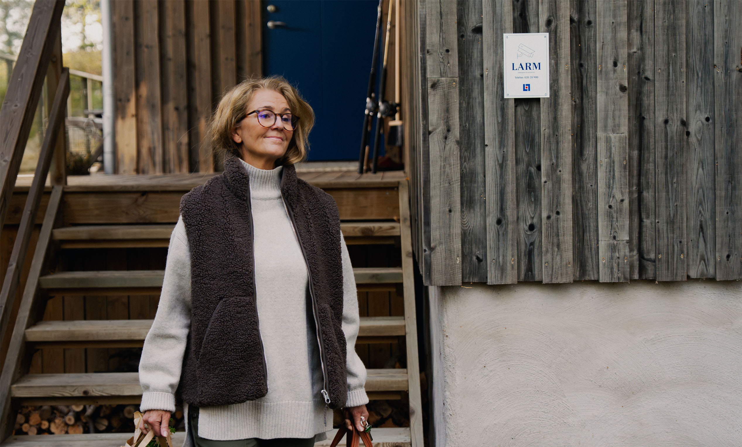 Kvinns som går ut från sitt fritidhus, i bakgrunden syns en larmskylt