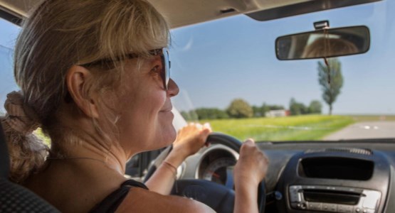 Kvinna kör bil på en landsväg i soligt väder.