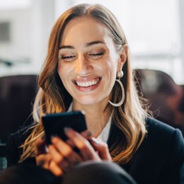 Ung, leende kvinna tittar ner i sin mobil.