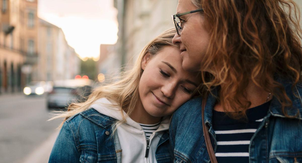 En mamma och hennes tonårsdotter kramar om varandra på stan.
