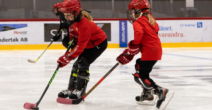 Två flickor i röda tröjor och hjälp lirar hockey