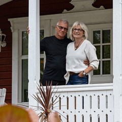 En kvinna och man står på sin veranda till sitt hus och tittar ut