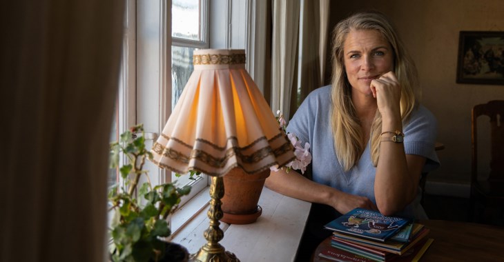 Författaren Emelie Sjölander sitter vid ett fönster med sina barnböcker intill sig.