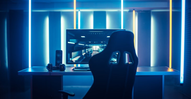 En ensam gamingdator och gamingstol i ett rum upplyst med blå lampor.