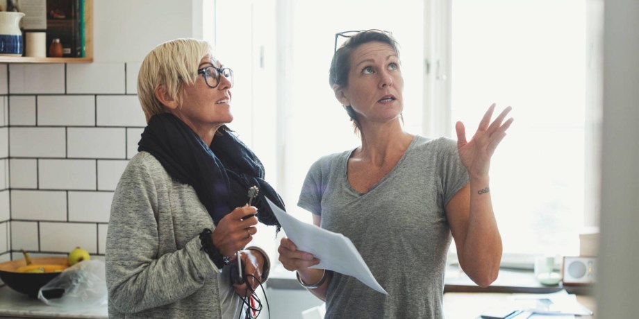 Två kvinnor står i ett kök och kikar upp mot taket.