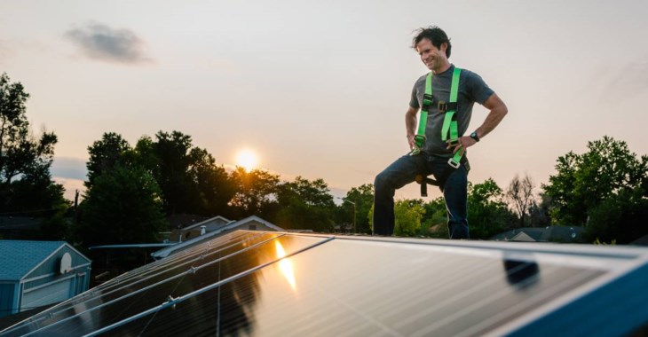 Installatör står på taknock och tittar ut över monterade solceller på ett tak.
