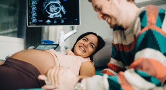 En gravid kvinna och hennes partner ler mot varandra under en ultraljudsundersökning.