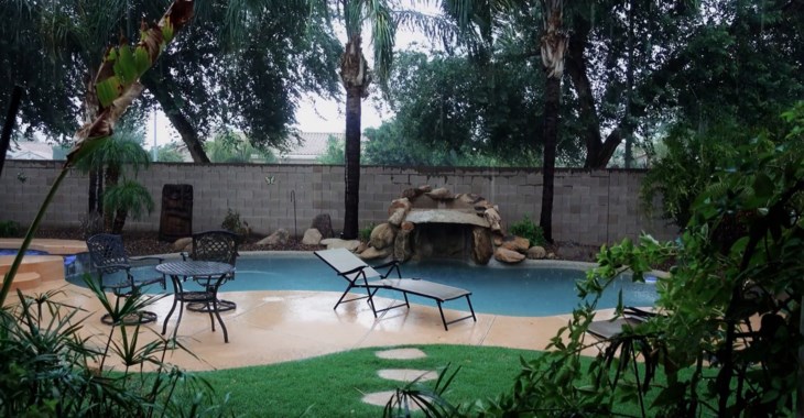 Regnet öser ned över ett poolområde med palmer.