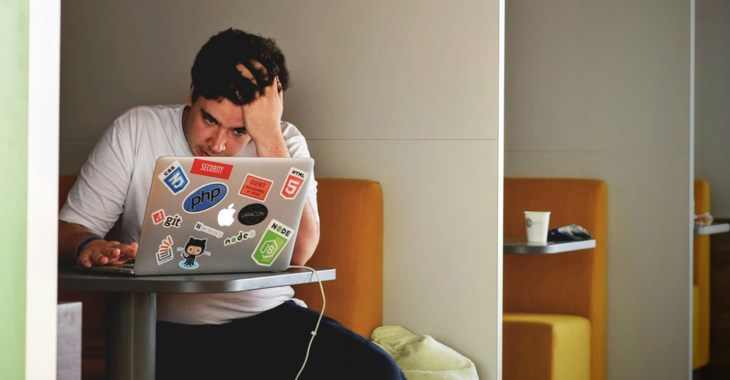 En kille sitter vid ett bord och kollar i sin dator.