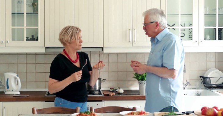 Ett äldre par står i ett kök och provsmakar mat.