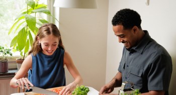 En ung kvinna och en ung man sitter vid köksbordet och hackar grönsaker till en gryta.