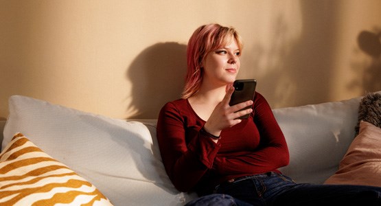 Kvinna sitter i soffan med sin mobil i handen.