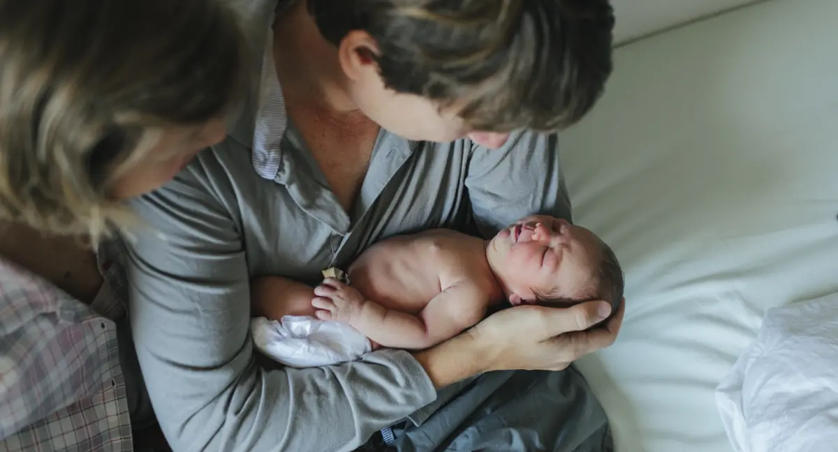 En nyfödd bebis vilar tryggt i föräldrarnas famn.