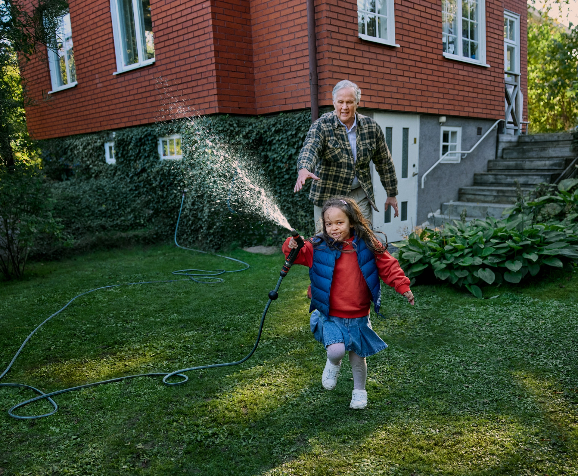 En morfar leker med sitt barnbarn i trädgården.