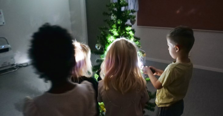 Flera barn står runt en gran och lyser upp reflexer
