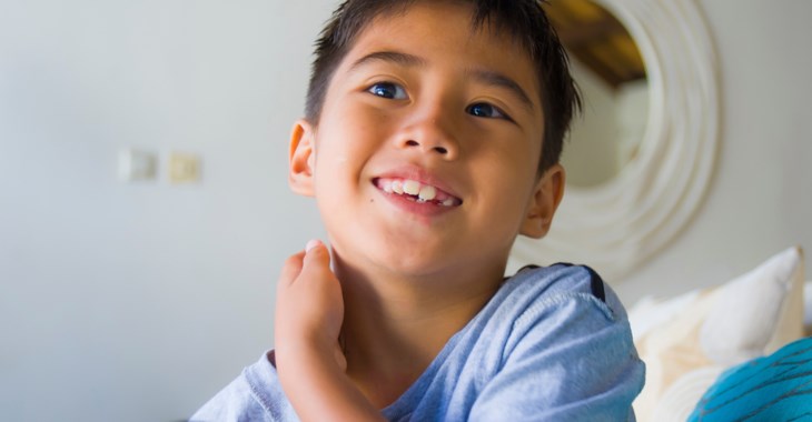 Pojke sitter i barnrum, ser glad ut.