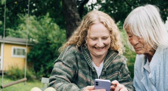 Ung kvinna tittar i mobilen tillsammans med sin farmor.