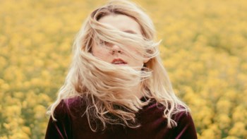 Flicka med vind i håret framför ett rapsfält.