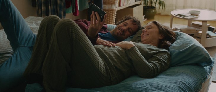 Par som ligger i en säng och kollar på en mobil.