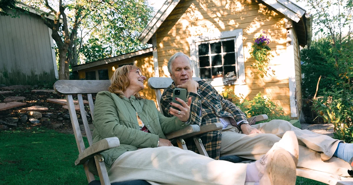 Ett par sitter utanför sitt fritidshus och tittar i mobilen tillsammans, fotografi. 