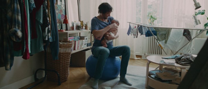 En nybliven pappa sitter på en pilatesboll och vaggar sin bebis.