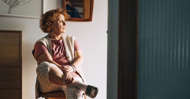 Kvinna sitter på stol hemma och tittar ut genom fönstret.