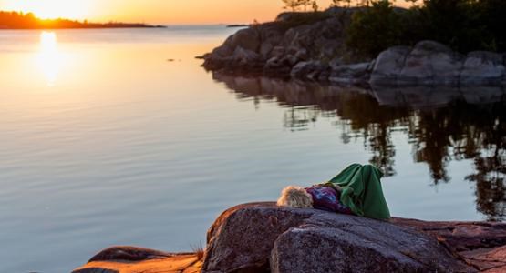 Kvinna ligger på ett berg i solnedgången. 