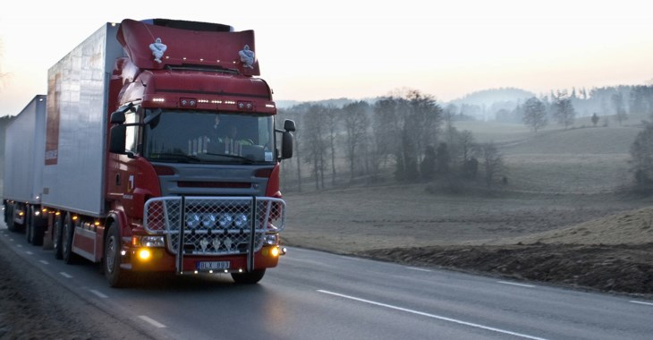 En röd tung lastbil dundrar förbi på en landsväg en disig vårmorgon någonstans i Sverige.