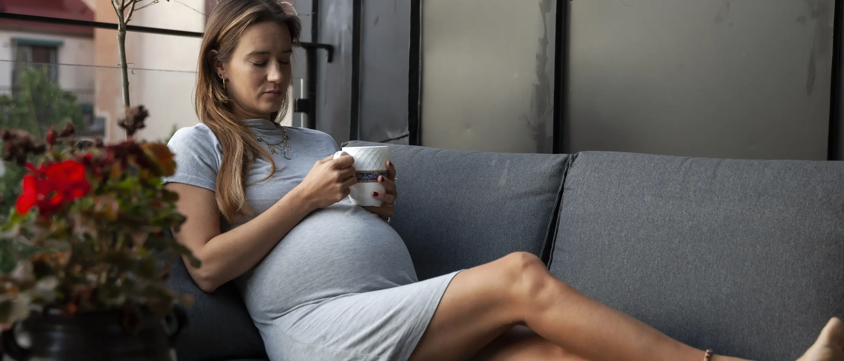 En gravid kvinna ligger med slutna ögon på en soffa på balkongen.