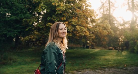 Kvinna i skogen med solljus.