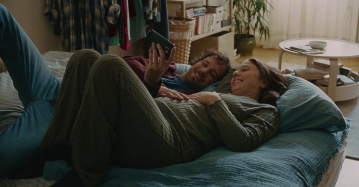 Par som ligger i en säng och kollar på en mobil.